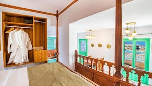 A bedroom with a wooden four-poster bed, a walk-in closet, and a view of the sea through a green door.