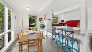 A modern kitchen with white cabinets, a red countertop, and a dining area with wooden chairs and a table.