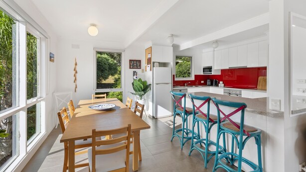 A modern kitchen with white cabinets, a red countertop, and a dining area with wooden chairs and a table.