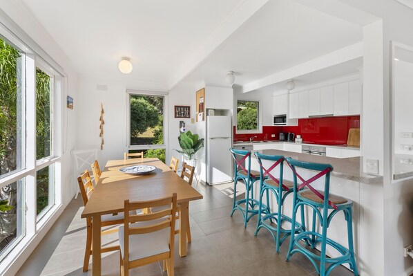 A modern kitchen with white cabinets, a red countertop, and a dining area with wooden chairs and a table.
