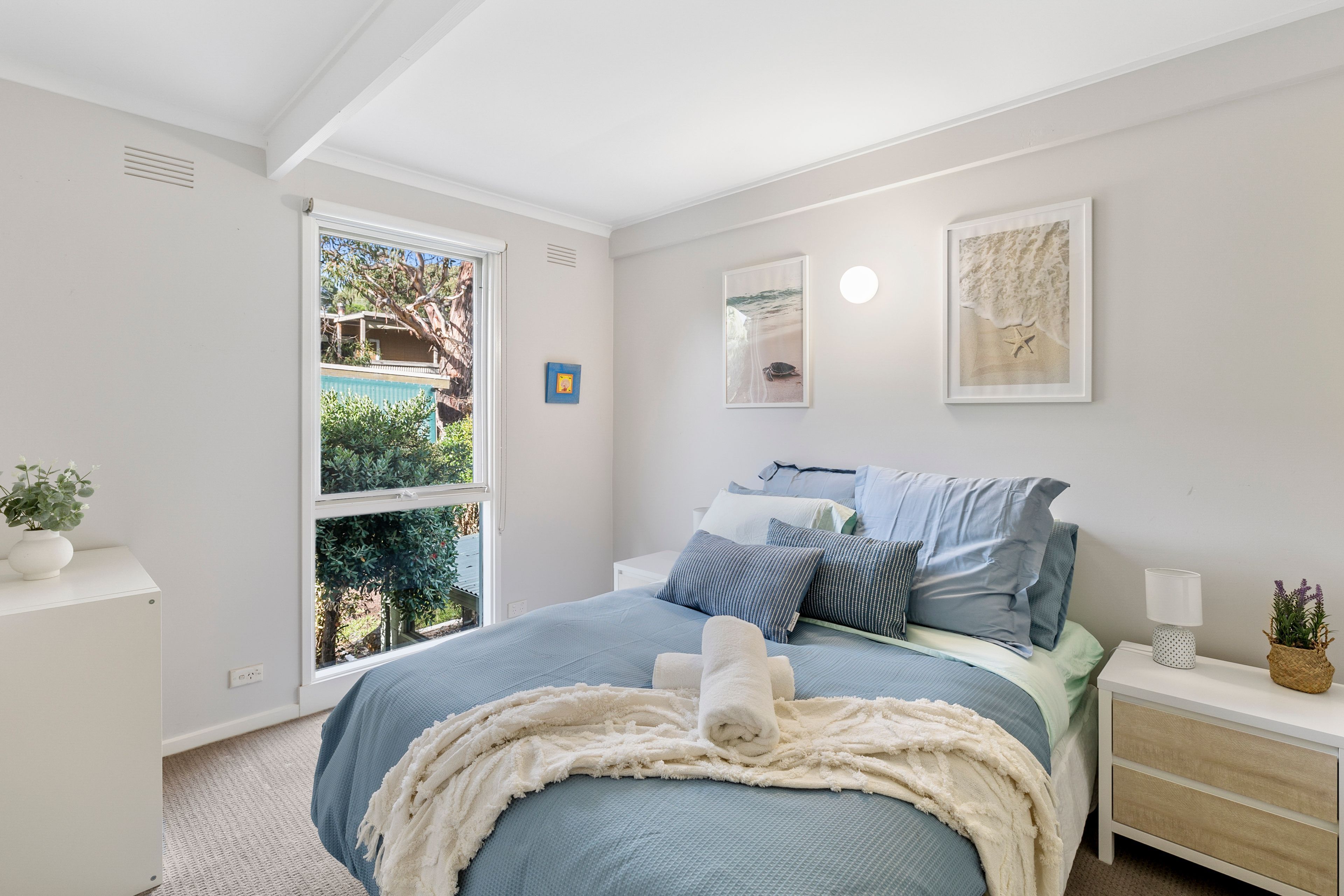 A bedroom with a bed, bedside tables, a window, and a wall-mounted picture.