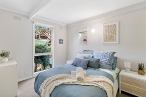 A bedroom with a bed, bedside tables, a window, and a wall-mounted picture.