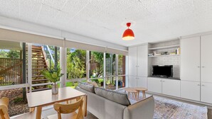 A modern kitchen with white cabinets, a built-in TV, and a dining area with a wooden table and chairs.