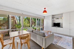 A modern kitchen with white cabinets, a built-in TV, and a dining area with a wooden table and chairs.