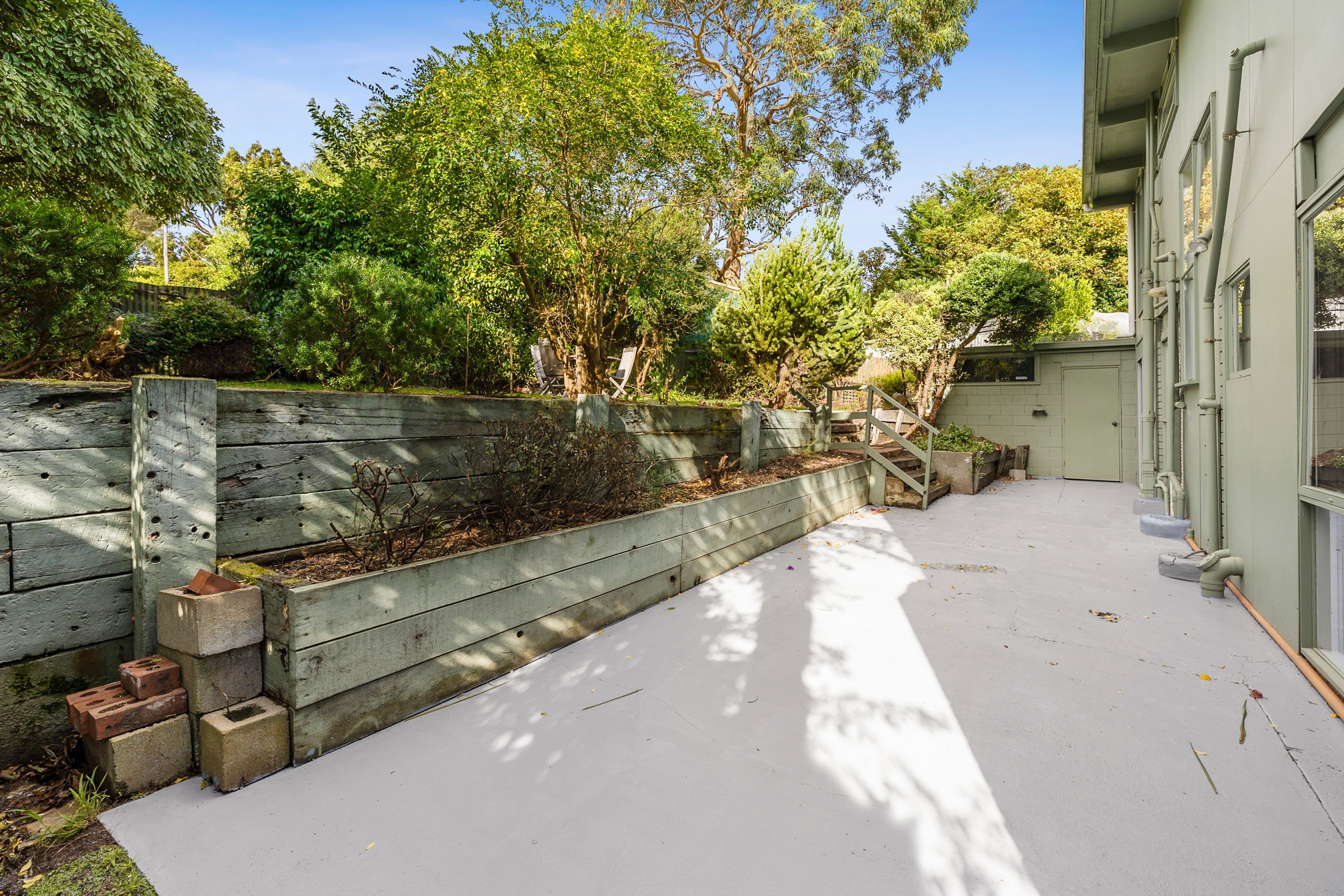 A paved outdoor area with a wooden fence, trees, and a building with windows.