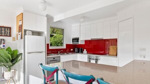 A modern kitchen with white cabinets, a red backsplash, and a large window.