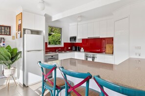 A modern kitchen with white cabinets, a red backsplash, and a large window.