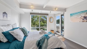 A bedroom with a large bed, a view of the outdoors, and a painting on the wall.