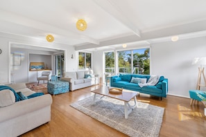 A spacious living room with a large blue sofa, a white sofa, and a beige sofa. There is a wooden coffee table in the center.