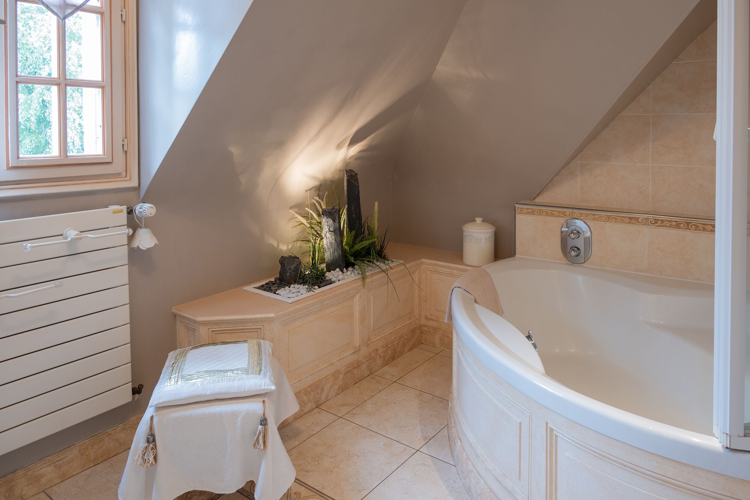 Un baño con una bañera, una mesita con una toalla y un ventanal con luz natural.