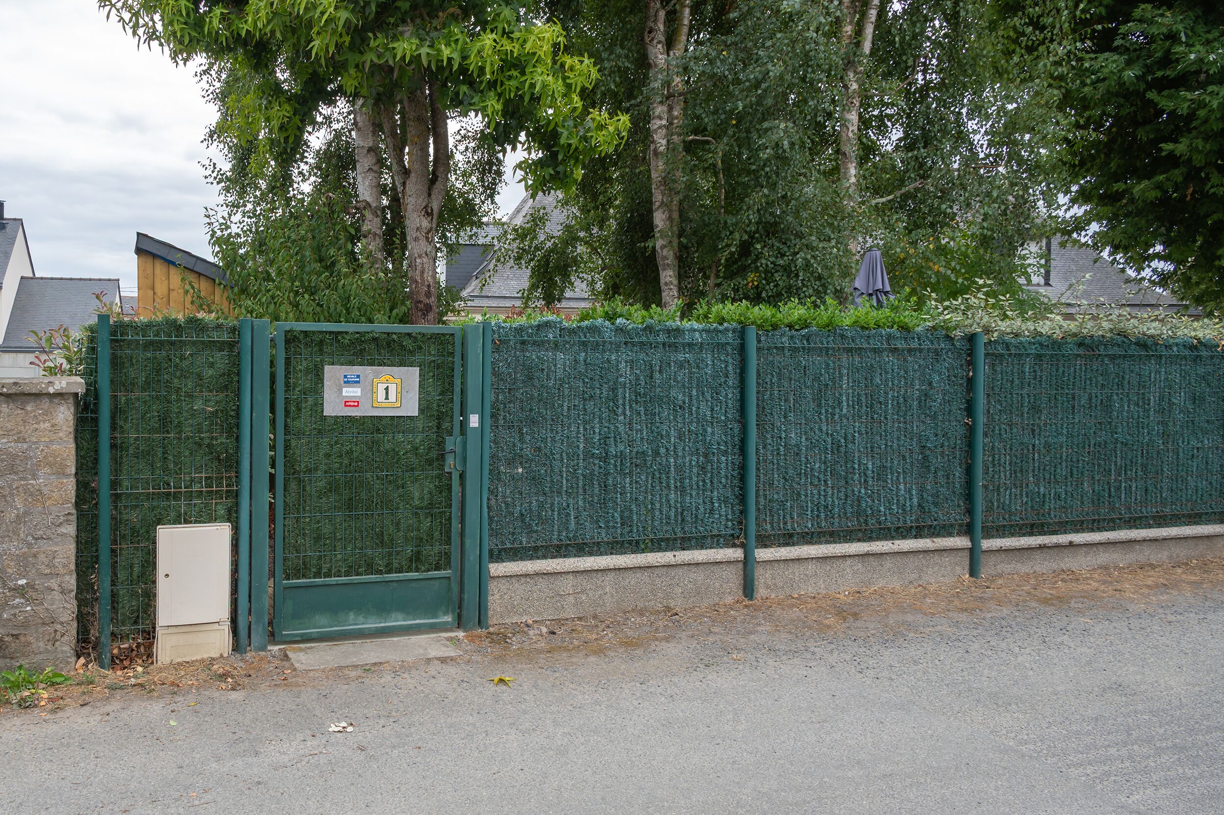 A green metal fence with a gate, a sign with the number 1, and a small utility box beside it.