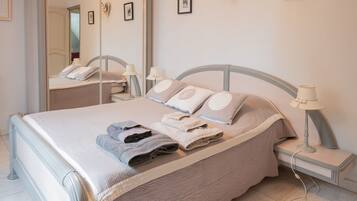 A neatly made bed with pillows and folded towels, a bedside lamp, and a mirror on the wall.