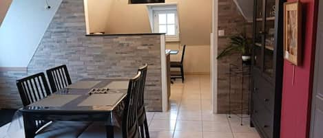A dining area with a table and chairs, a kitchen with cabinets, and a red accent wall.