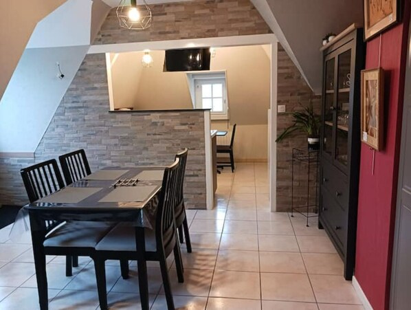 A dining area with a table and chairs, a kitchen with cabinets, and a red accent wall. - Cancale - Côte D'émeraude (Cancale)
