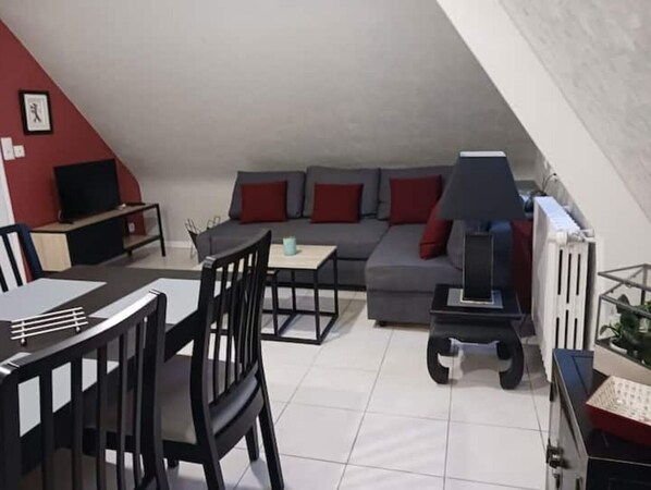 A modern living room with a grey sofa, red cushions, a small table, and a TV. - Cancale - Côte D'émeraude (Cancale)