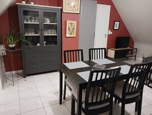 A dining area with a table and chairs, a cabinet with glass doors, and a television on a stand. - Cancale - Côte D'émeraude (Cancale)