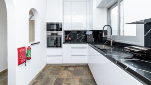 A modern kitchen with white cabinetry, a black countertop, and a fire extinguisher mounted on the wall. - Blossom Holiday Villa DPS18 (Paralimni)