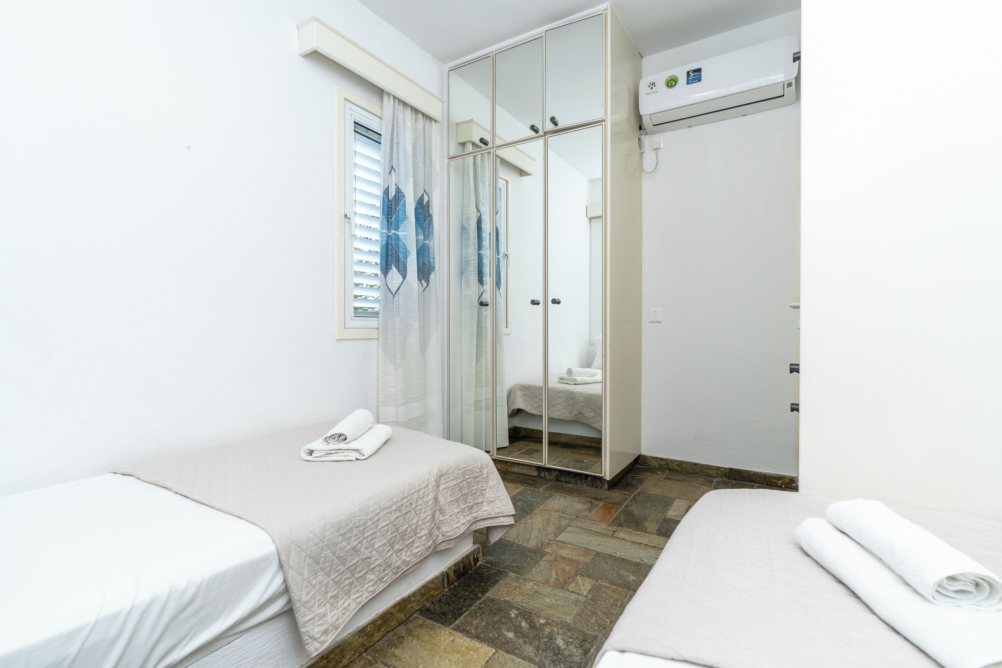 Habitación de hotel con dos camas, cabina de ducha de vidrio y aire acondicionado blanco.