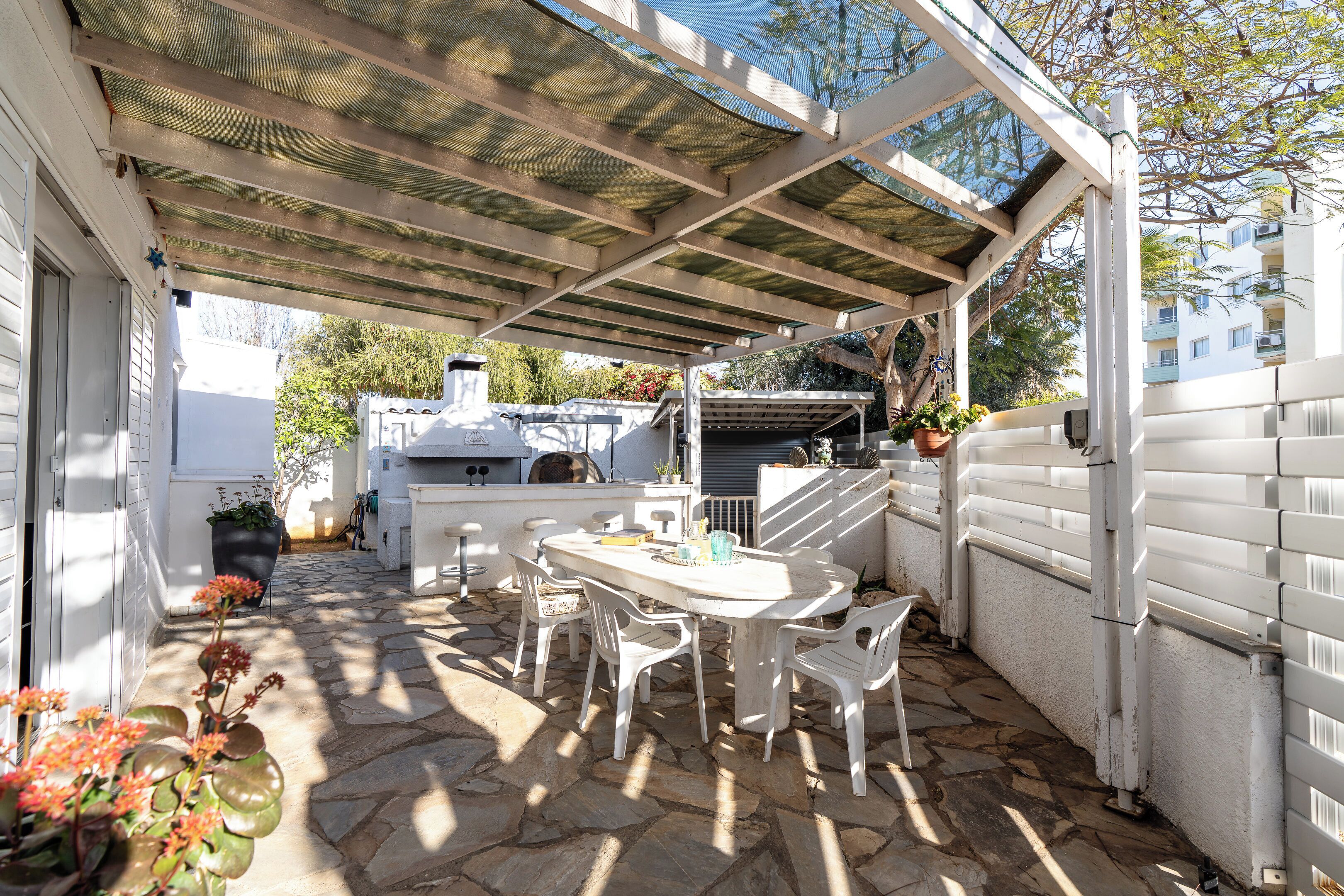 A covered patio with a stone floor, white furniture, and a grill area.
