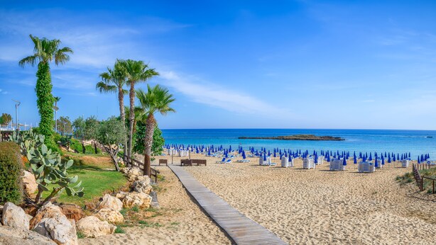 A beach with a wooden walkway, palm trees, and blue umbrellas. - Blossom Holiday Villa DPS18 (Paralimni)
