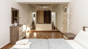 A bedroom with a wooden floor, a bed with a patterned bedspread, a dresser, a mirror, and a wardrobe with a mirror. - Blossom Holiday Villa DPS18 (Paralimni)