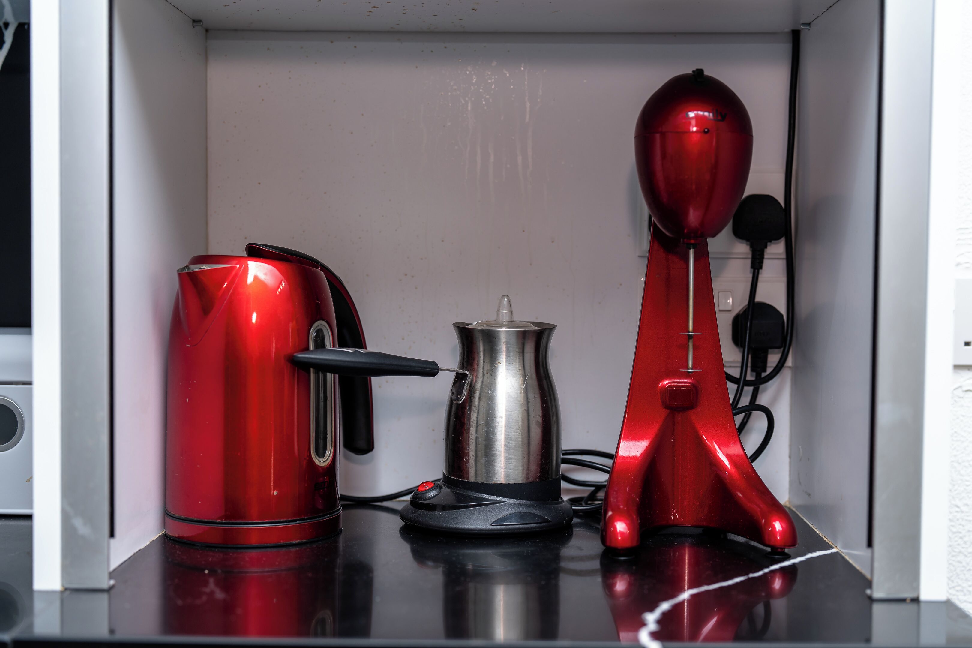 A kitchen with a red kettle, a silver pot, and a red electric kettle on a black countertop.