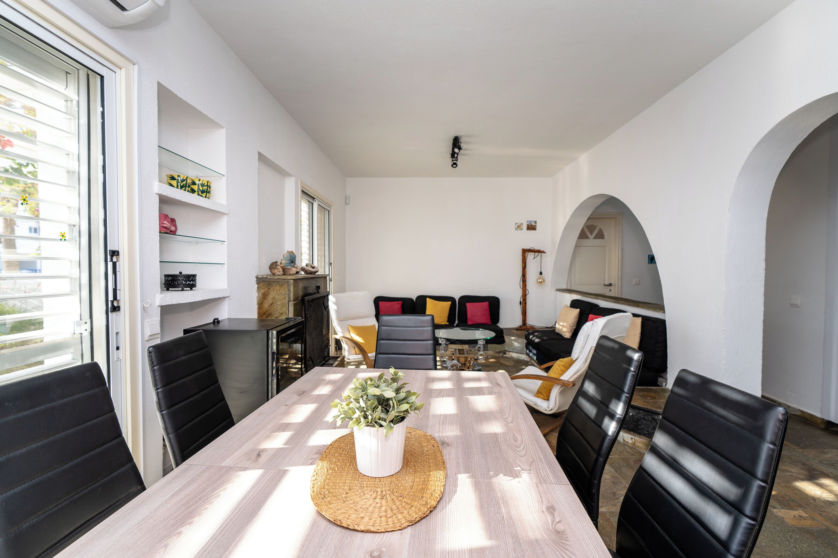 A dining area with a wooden table, black chairs, and a woven placemat. There is a potted plant on the table.