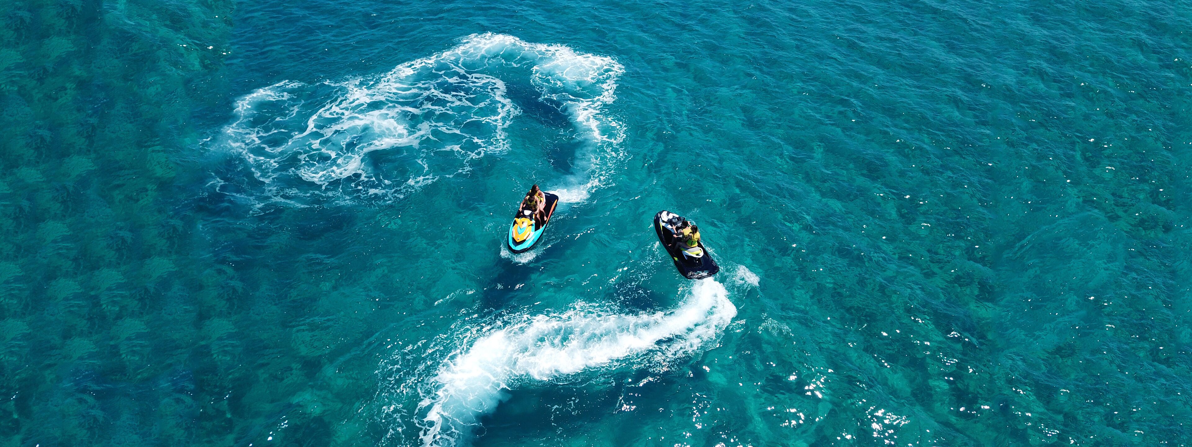 Two jet skis on a clear blue water body.