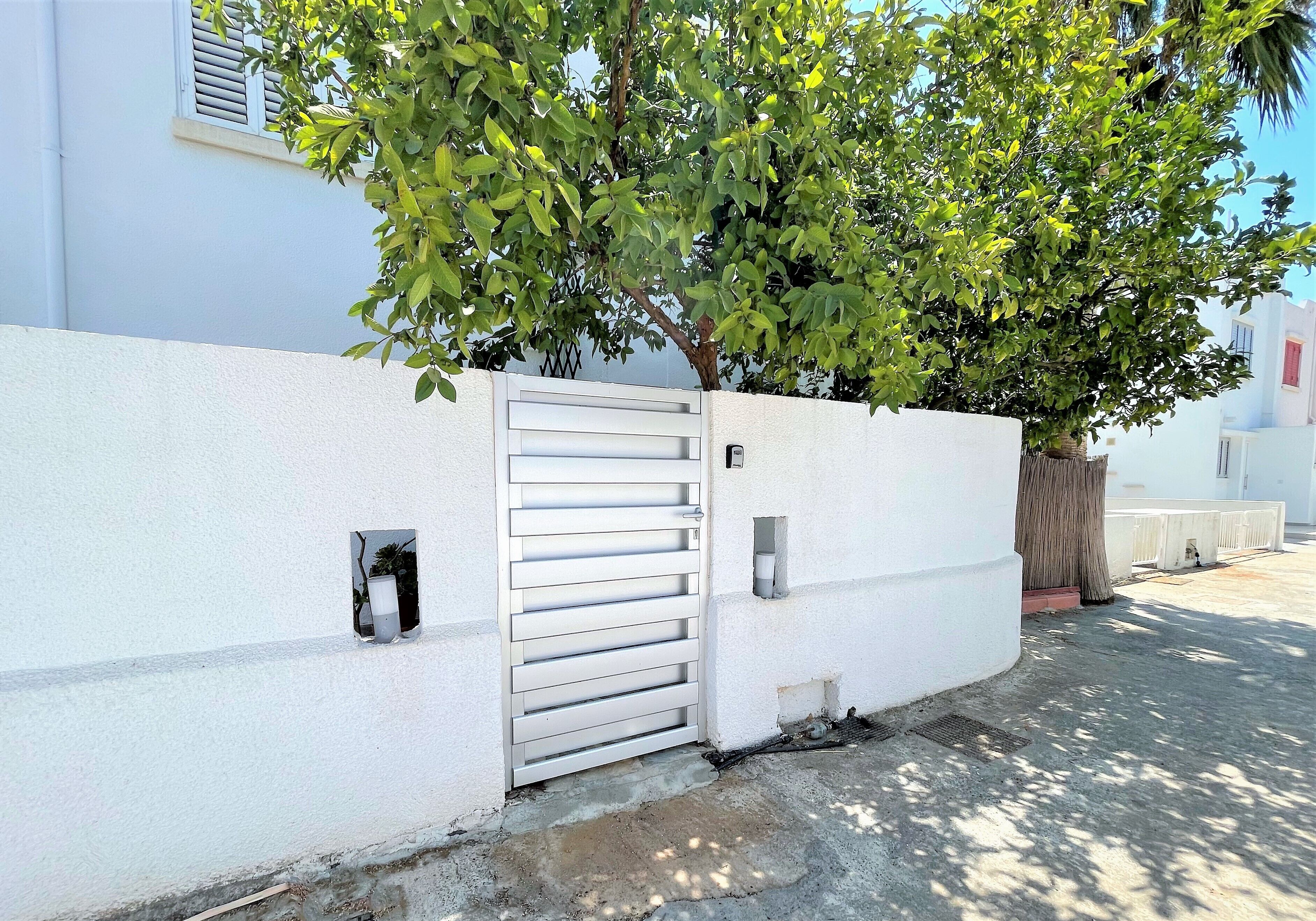A white wall with a metal gate, a tree, and a small window.