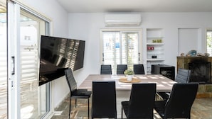 A modern dining area with a large table, black chairs, a flat-screen TV mounted on the wall, and a fireplace. - Blossom Holiday Villa DPS18 (Paralimni)