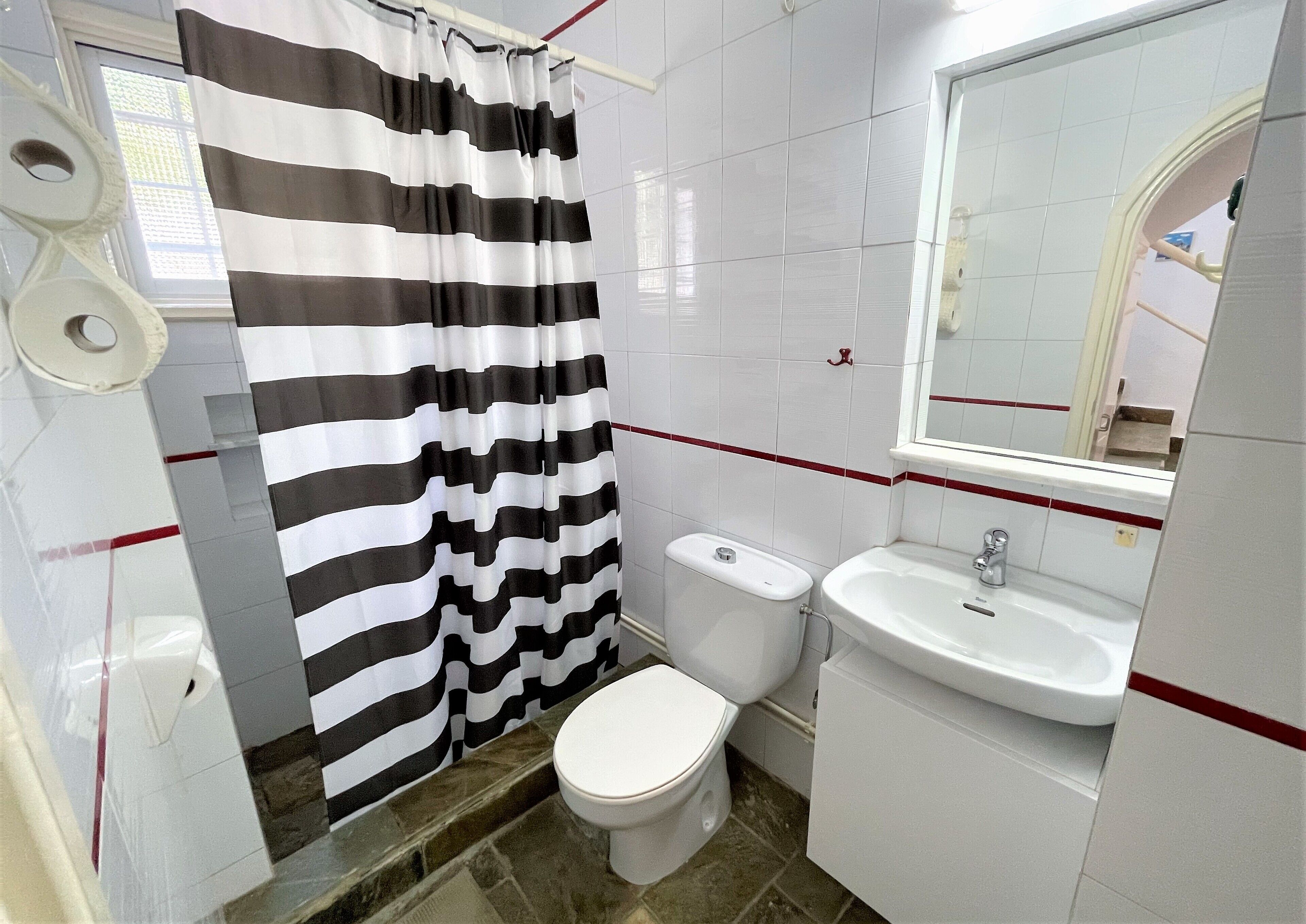 A bathroom with a striped shower curtain, a toilet, a sink, and a mirror.