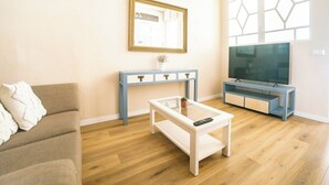 Una sala de estar con sofá, mesa de centro, mueble para TV y un ventanal con diseño geométrico.