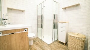 Un baño moderno con cabina de ducha de vidrio, inodoro blanco y tocador de madera.