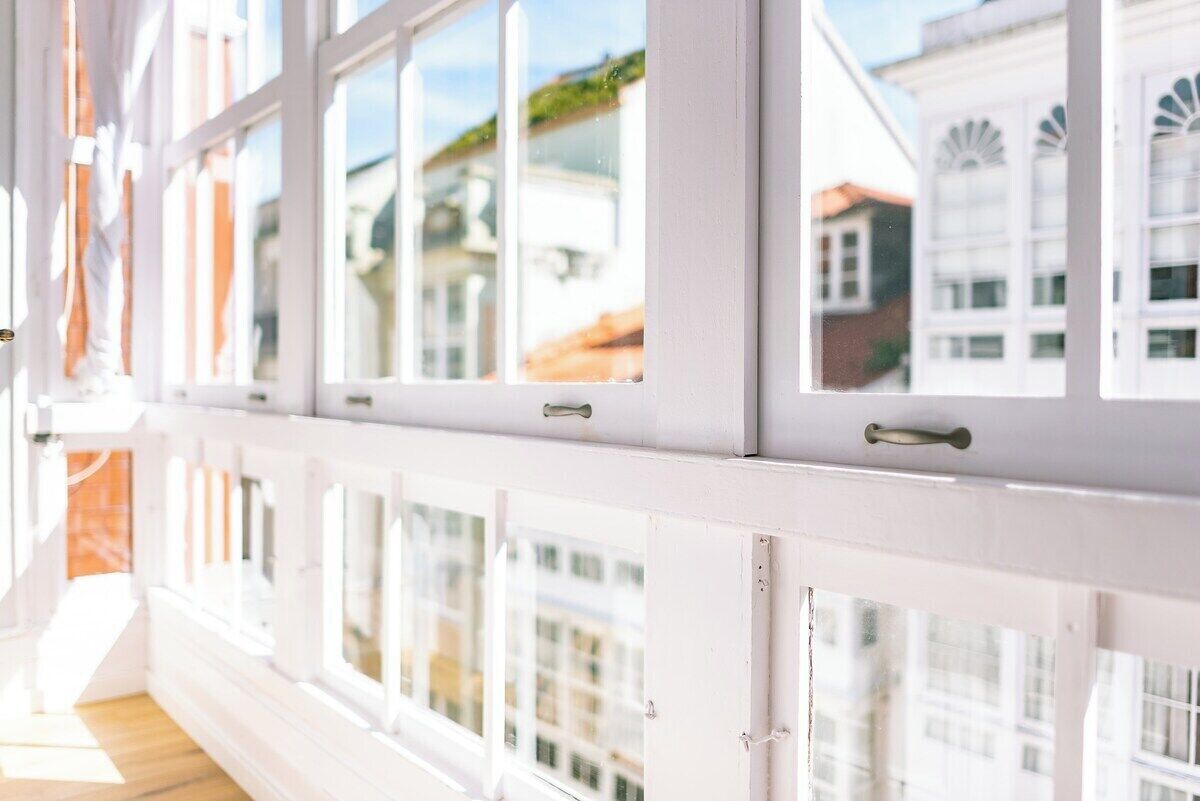 A corridor with white walls and large windows, leading to a room with a view of buildings outside.