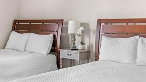 A hotel room with two beds, each with a wooden headboard and white bedding. There is a small bedside table with a lamp and a vase of flowers between the beds. - Spacious 5 Bedroom Dallas Home for Families (Dallas)