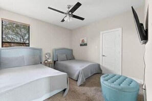 A bedroom with two beds, a ceiling fan, a TV mounted on the wall, and a door.