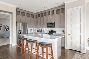 Una cocina moderna con una isla grande, electrodomésticos de acero inoxidable y taburetes de bar de madera.