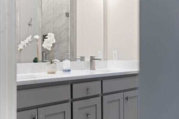 Un baño con un espejo grande, un lavamanos blanco y un mueble debajo.