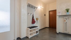 Un couloir avec un banc blanc, des patères, un panier fixé au mur et une porte.