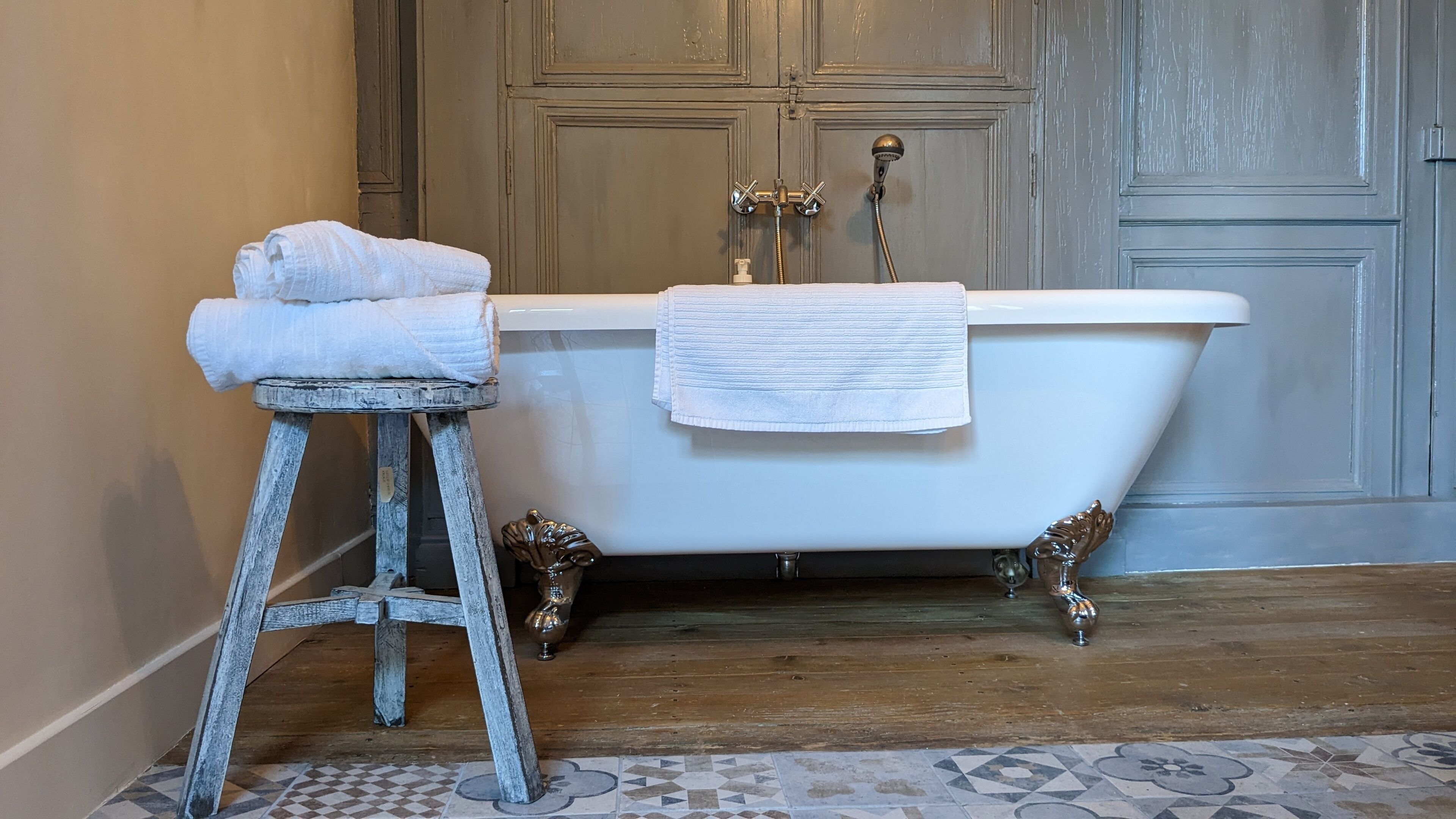 Casa de banho com banheira de patas de leão, um banquinho de madeira com toalhas e um chuveiro de estilo vintage.
