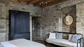 Un dormitorio con pared de piedra, un armario de madera oscura, cama con estructura metálica y un espejo redondo.