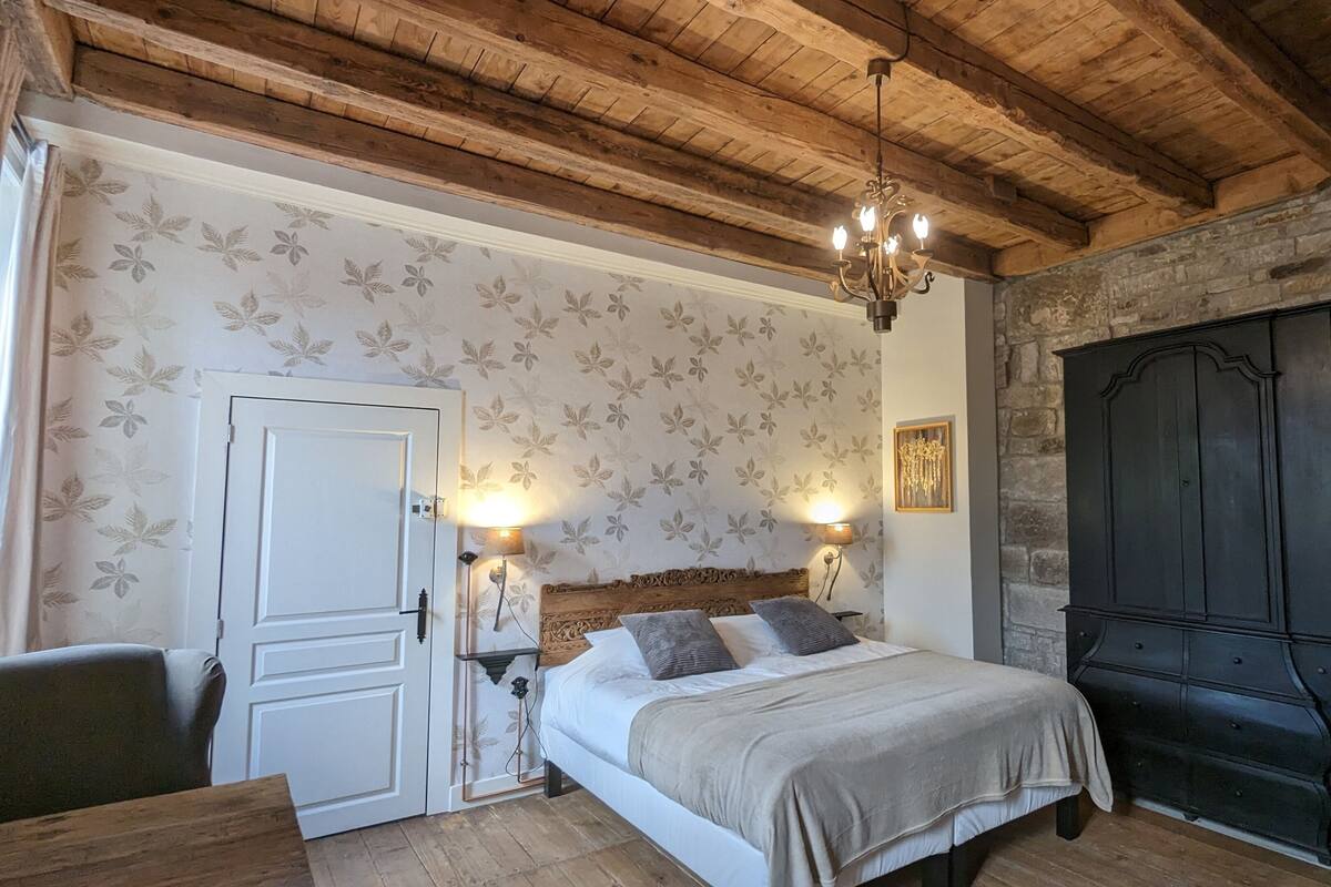 Ein Schlafzimmer mit Holzbalkendecke, einem Bett mit Kopfteil, einem Kleiderschrank und einer Wandleuchte.