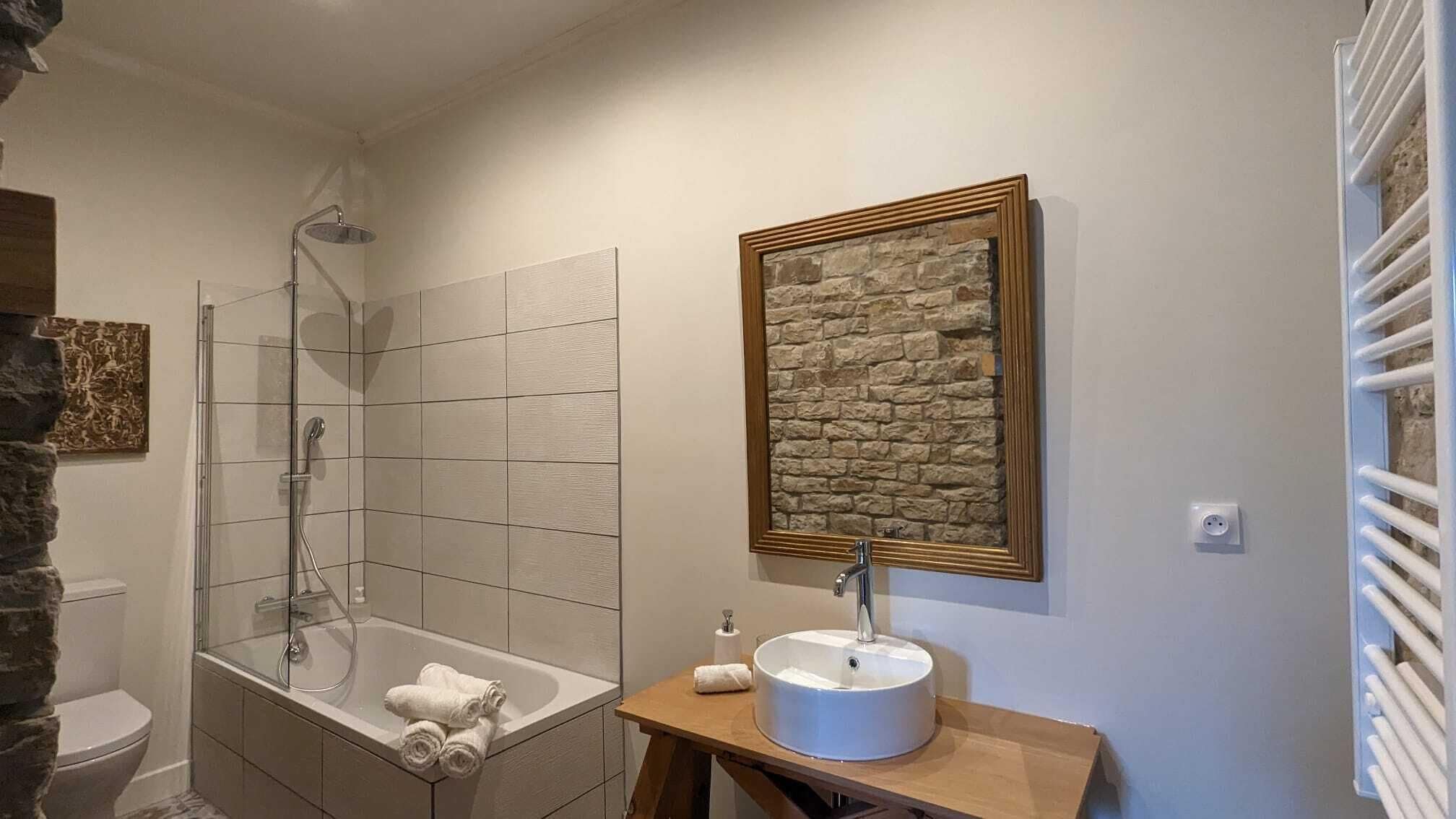 A bathroom with a glass-enclosed shower, a white sink with a stone backsplash, and a wooden vanity.