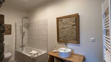 A bathroom with a glass-enclosed shower, a white sink with a stone backsplash, and a wooden vanity.