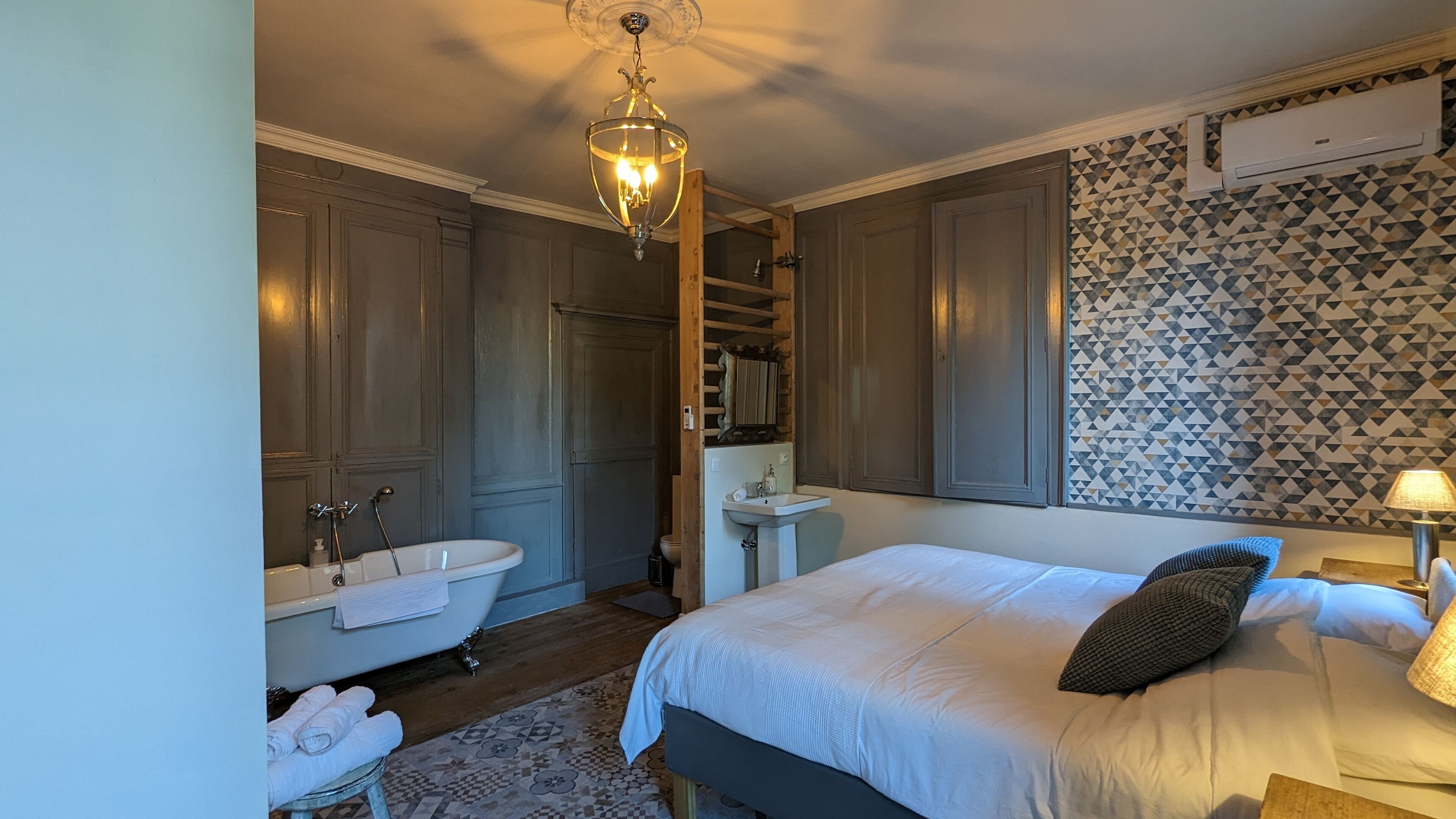 Ein Schlafzimmer mit Bett, Nachttisch, Lampe, Kommode, Schminktisch mit Spiegel, Badewanne und Dusche.
