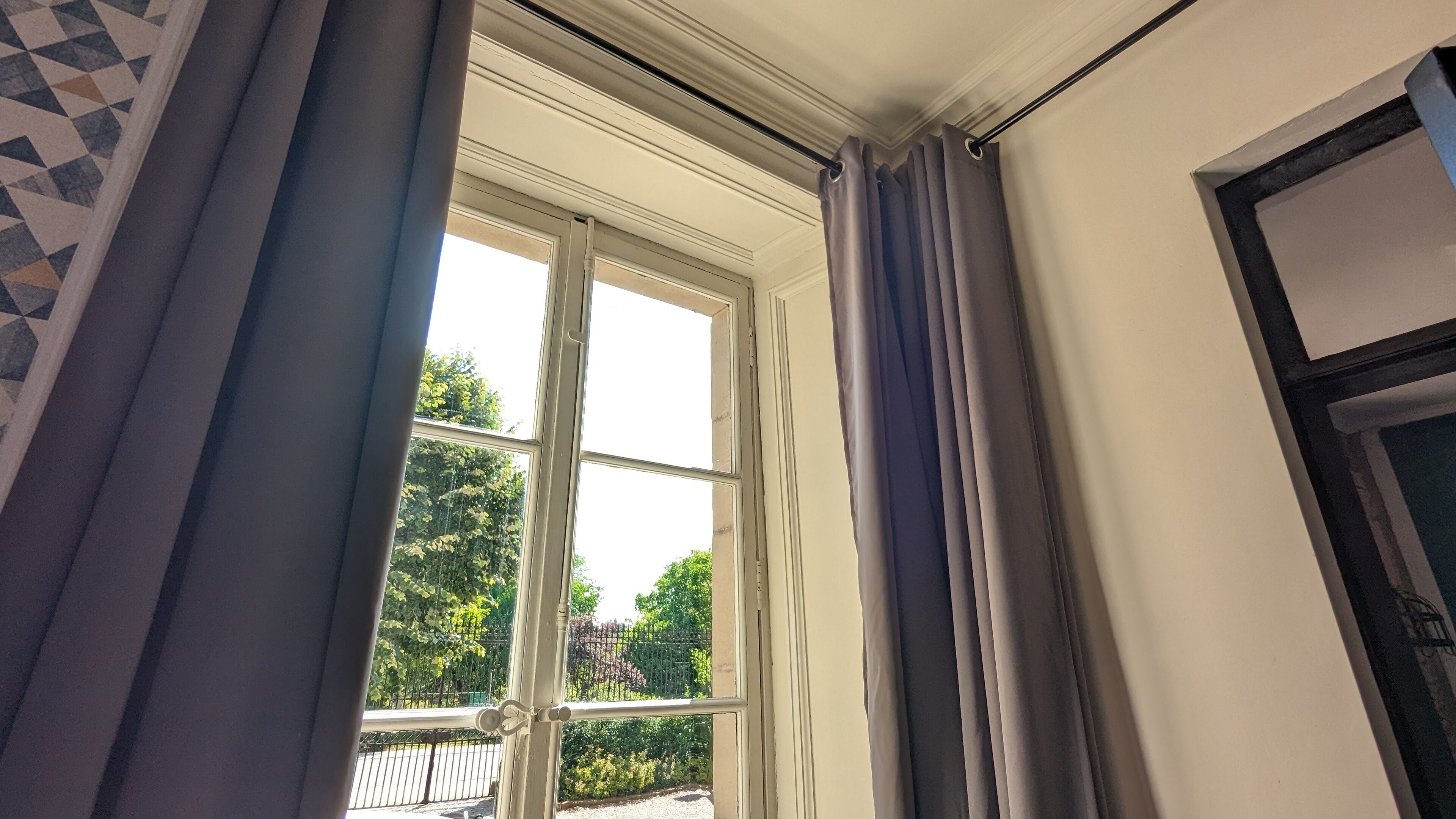 A room with a large window, curtains, and a view of greenery outside.