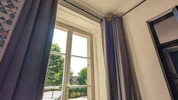 A room with a large window, curtains, and a view of greenery outside.