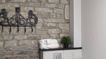 A bathroom with a stone wall, a white toilet, a black trash bin, and a towel rack with a towel and a plant.
