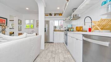 A modern kitchen with white cabinetry, a stainless steel dishwasher, and a wooden drying rack.