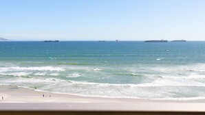 Een strand met golven en schepen in de verte.